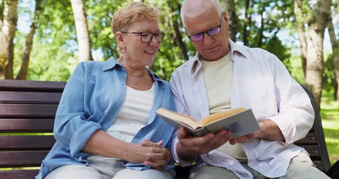 Seniors couple reading book in outdoor park. On a bench they share calm relaxation, enjoying stories and leisure together in soft outdoor light. Theme of love romance learning connection.