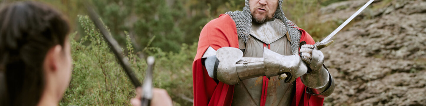 Header of middle aged CaucLatin knight in steel armor holding sword fighting opponent outdoors. Action visual suitable for historical festival promotion and gaming marketing