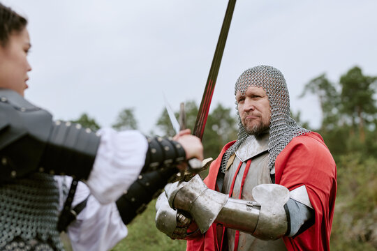 Middle aged CaucLatin man and young Latin woman in knight armor fighting with swords outdoors. Concept representing historical reenactment, conflict resolution, or fantasy gaming marketing