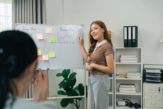 Young woman giving presentation on business growth with charts and sticky notes while colleague listens in modern office room