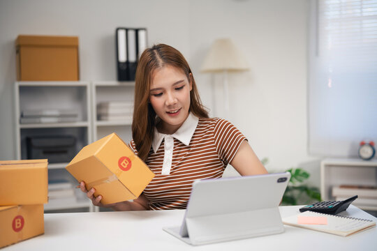 Young woman working at home packing delivery box and using digital tablet for online business or ecommerce order processing