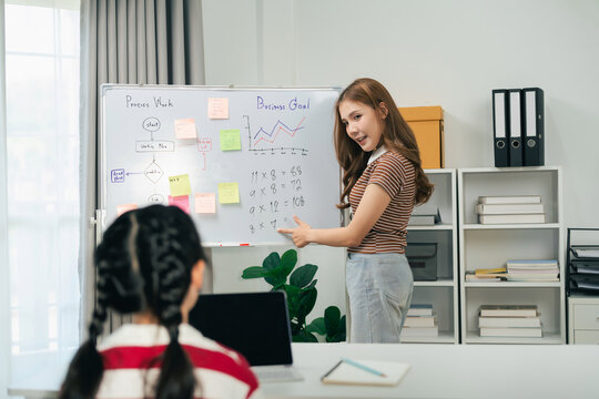 Young girl presenting math problems and business chart on whiteboard in modern classroom setting with student listening