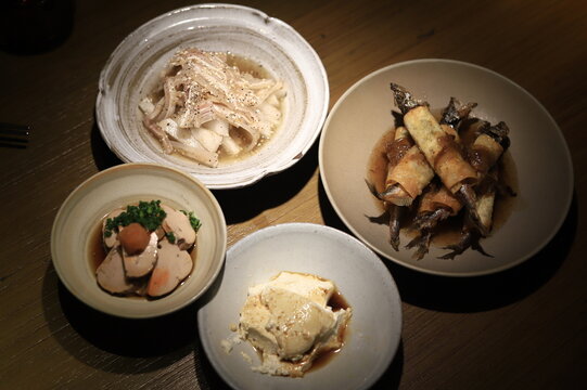 Close-up of four traditional Japanese appetisers including Tofu, Fish spring rolls, foie gras and Pickled white radish strips on a table