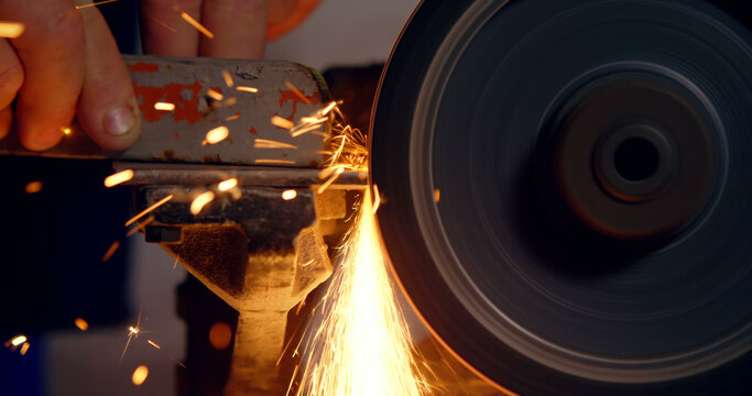 A worker sharpens metal on a grinding wheel, with copy space