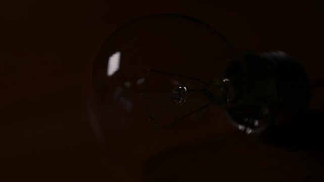 Incandescent light bulb blinking and flickering in the dark. Close-up of a glass incandescent bulb with a reddish filament blinking and glowing in the dark, power fluctuations or malfunction