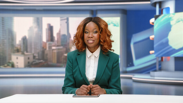 Portrait of a Black Female News Anchor Presenter Hosting the Evening Bulletin From the Studio Desk, Breaking Story Segments and Addressing Viewers Directly During a Live Television News Broadcast.
