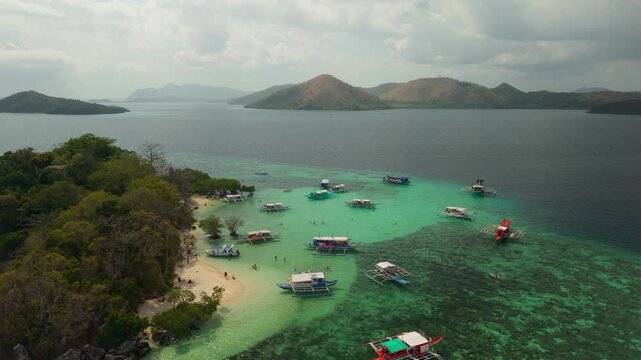 Aerial drone footage of CYC Beach in Coron, Palawan, Philippines, featuring traditional Filipino outrigger boats anchored in shallow turquoise waters beside a small white sand beach 