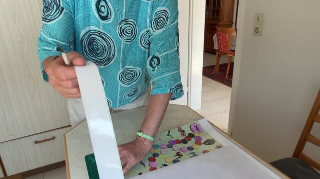 Woman continues trimming a large printed poster and pulls away the cut border by hand. Because the paper edge is not completely separated, she gently tears the remaining section to remove the strip.