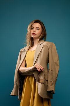 Composed woman wearing beige blazer over mustard dress against teal studio background. Business casual, personal branding, career fashion concept.