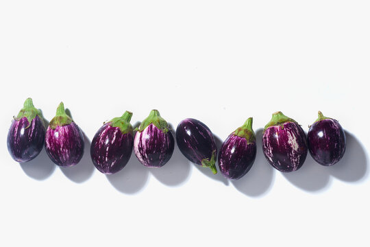 Row of Purple and white striped aubergines on white background