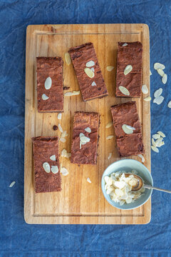 Brownies topped with sliced almonds on wooden cutting board