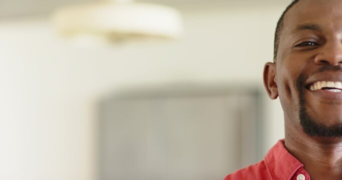 Mid-adult African American man smiling, wearing red shirt at home near pendant lamp, copy space