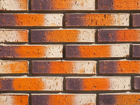 Fragment of strong wall, close-up. Masonry clinker bricks characterized by bands of dark brown, orange, and light (engobed) shades. Decorative surface intended for building facades, interior finishes.