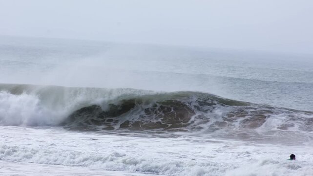 After a quick reframe, a wave at Supertubos beach throws a hollow barrel laced with offshore spray and explodes, a tiny bodyboarder's head bobbing in the foreground foam.