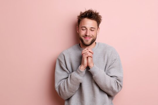 Portrait of a glad man in his 20s joining palms in a gesture of gratitude in pastel or soft colors background