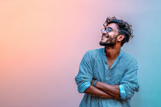 Portrait of a jovial indian man in his 20s with arms crossed over pastel or soft colors background