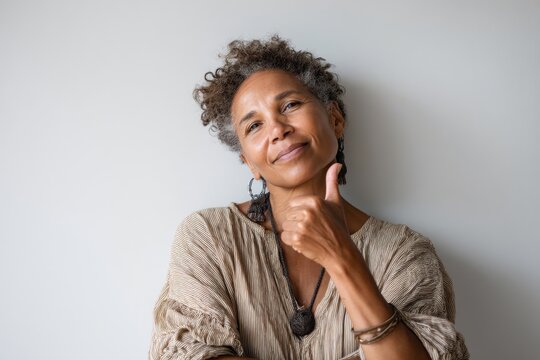 Portrait of a content afro-american woman in her 50s showing a thumb up while standing against minimalist or empty room background