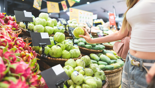 Young adult asian woman customer supermarket shopping cart choosing guava fruits products grocery food at department store