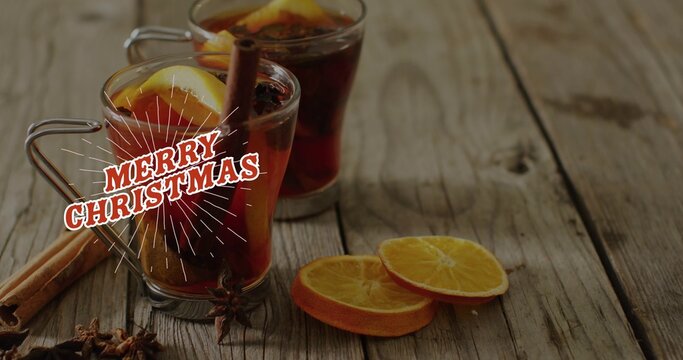 Two glass mugs holding dark red drink with star anise and Christmas overlay on wooden tabletop