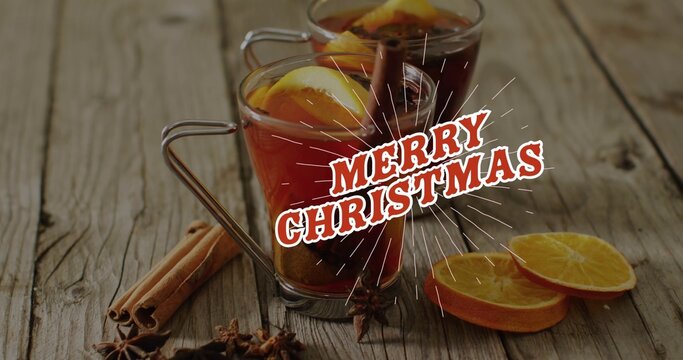Two glass mugs holding dark red spiced drink with orange slices beside MERRY CHRISTMAS on table