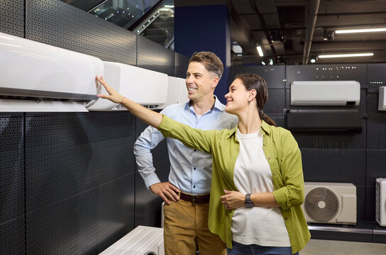 Couple customers choosing appliances in retail store. They evaluate a wallmounted unit together and smile. Positive buying mood in a bright showroom. Clear consumer purchase decision concept.