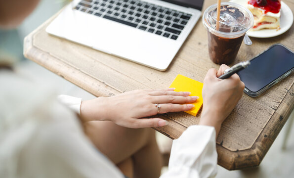 Closeup hand young adult  business woman using pen writing note for study, work online workplace cafe table with lapto