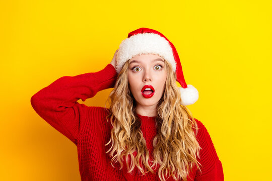 Surprised woman in Santa hat and red sweater against bright yellow background expressing holiday shock and festive fun