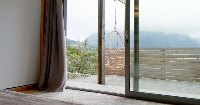 Wicker chair hanging on wooden deck beam overlooking misty mountain hills through sliding door