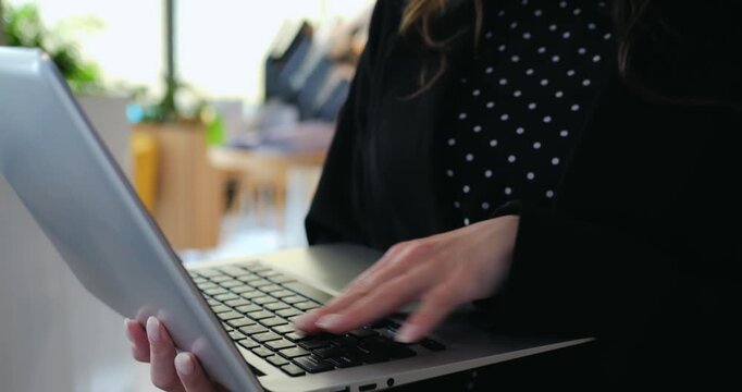 Professional specialist holding portable laptop types project updates inside bright contemporary office. Focused businesswoman performs daily administrative work and communication efficiently.
