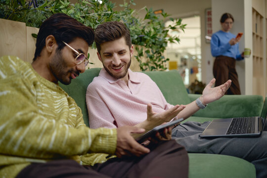 Diverse young adult business colleagues discussing project on digital tablet and laptop in coworking office. Useful for corporate collaboration and technology marketing campaigns