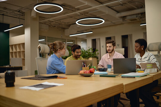Diverse group of young adult business colleagues collaborating with laptops in coworking office. Commercial image suitable for corporate teamwork and modern workplace marketing