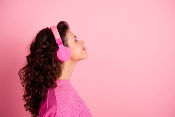 Young woman wearing pink headphones listening to music with eyes closed, relaxed profile portrait against pink background conveying joy and lifestyle © deagreez