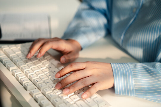 Close-up of an office professional in a blue striped shirt typing on a white computer keyboard at a desk, with paperwork in the background, illustrating data entry, office work and productivity.