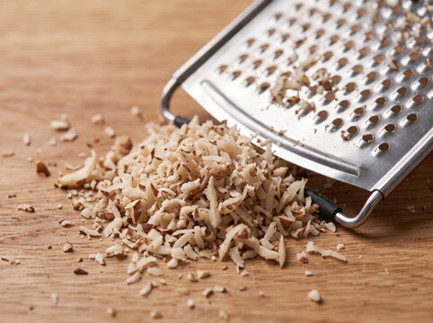 Finely grated hazelnut shavings on wooden board with metal grater