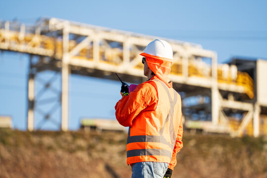 Industrial worker in protective gear communicating by radio beside steel infrastructure