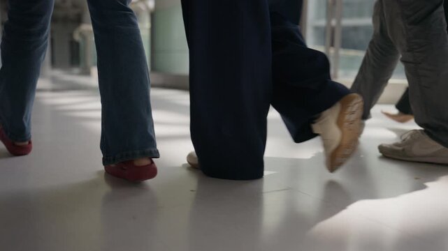 Close-up low angle view of business professionals walking with digital tablets and documents along a glass corridor, representing workplace mobility, modern technology, teamwork, and corporate life.