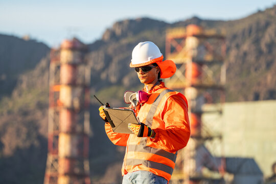 Mining worker in high-visibility gear, reviewing a tablet at a mountain worksite