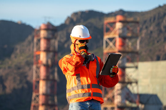 Industrial engineer checking a tablet while communicating by radio at a power facility