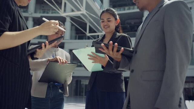 Asian business professionals discussing work while using digital tablets and documents in a modern workplace, representing digital transformation, technology adoption, collaboration, and business effi