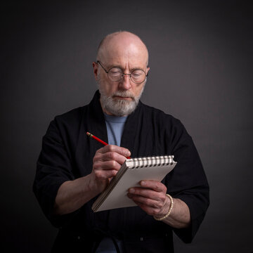 Portrait of bald and bearded senior man sketching or writing with a pencil in a notebook