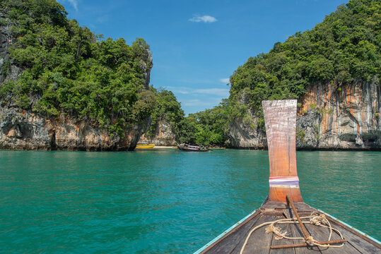 Traditional longtail boat prow heading into emerald lagoon surrounded by limestone karst cliffs in Thailand
