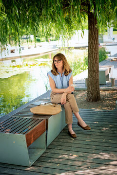 Middle-aged blonde woman drinking iced coffee on a park bench on a summer day