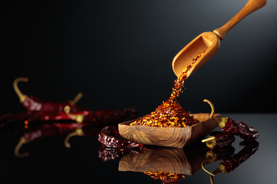 Dry red chili peppers and crushed chili flakes on a black reflective background.