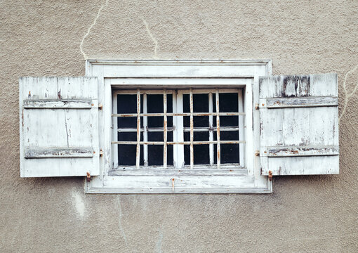 Old multi-pane window with iron grid and wooden shutters. Historic white painted frame with peeling paint and crack repair. Rustic Swiss architecture detail. Lucerne, Switzerland. Selective focus.