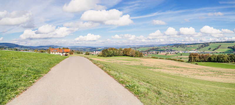 Swiss autumn countryside panorama. Rural road leading to farmhouse with village and rolling hills with blue sky with cumulus clouds. View toward Berom&uuml;nster, Lucerne, Switzerland. Selective focus.