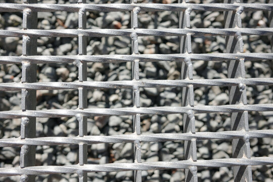 Close-up pattern of industrial metal grate floor over gravel background