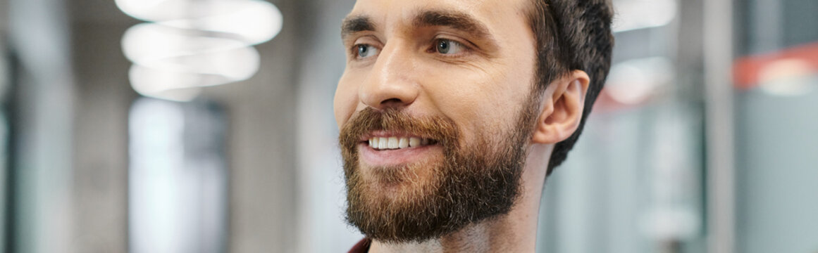 A bearded young man smiles in a bright contemporary workspace during the workday.