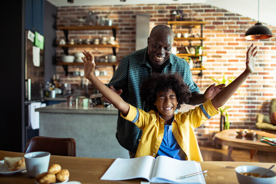 Child celebrates homework success with supportive adult in kitchen