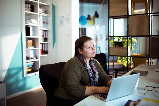 Thoughtful woman looking away from laptop at office desk