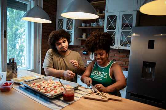 Couple preparing mini pizzas together in home kitchen